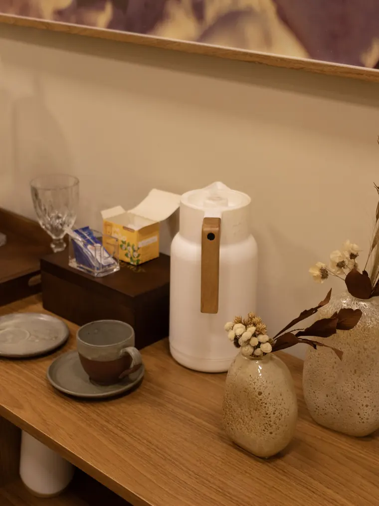 Aparador de madeira na área de espera da RYO Spa, com jarra, xícaras e arranjo de flores secas